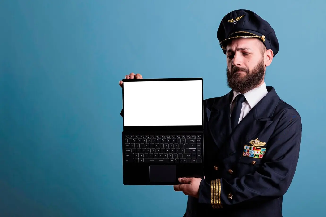 Ernster Flugzeugpilot zeigt einen Laptop mit weißem, leerem Bildschirm, Werbung für Software einer Luftfahrtakademie, PC mit Mock-up einer Flughafen-Website. Flugkapitän hält einen tragbaren Computer mit leerem Display.