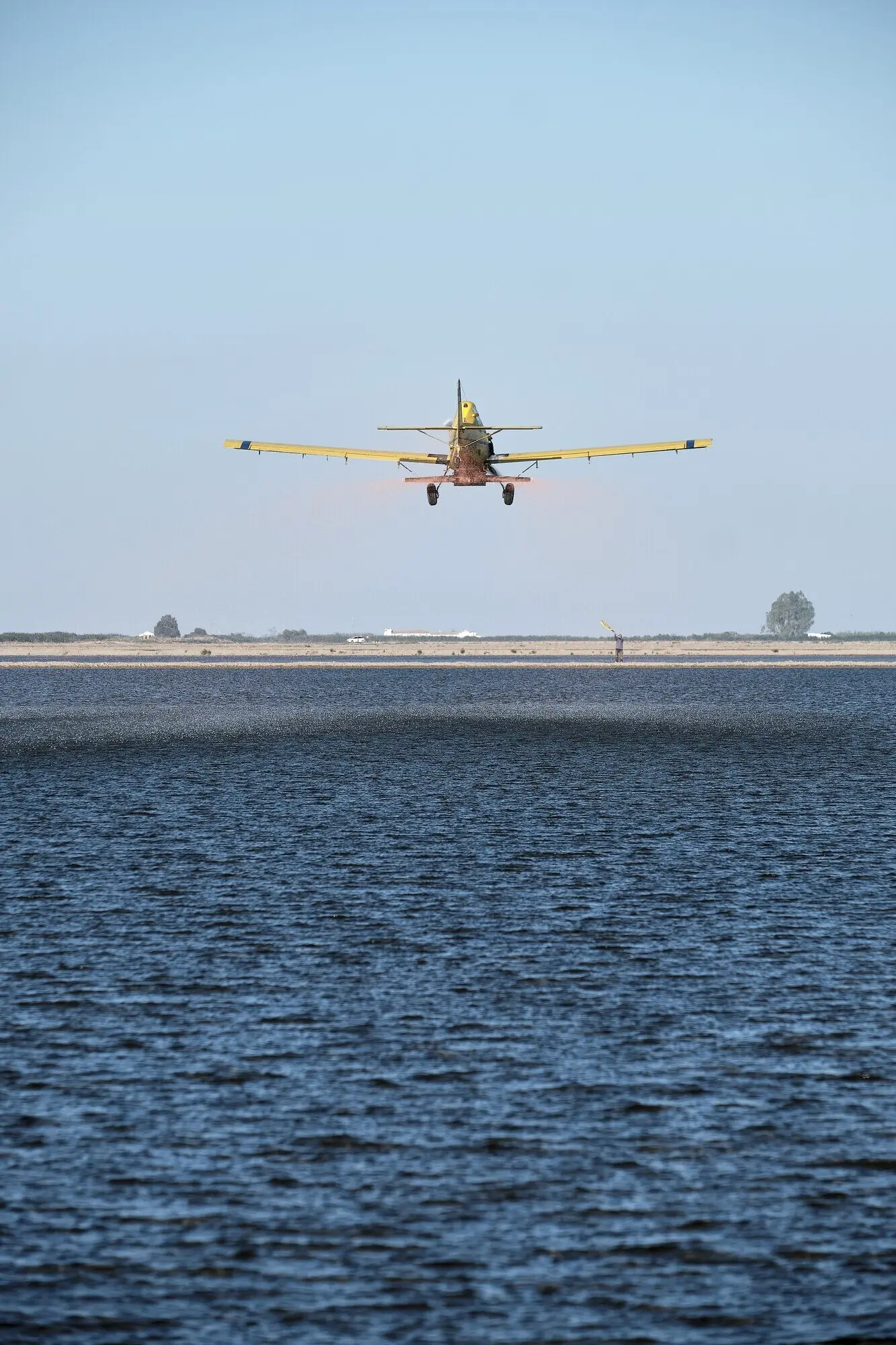 Hochformataufnahme eines klassischen einmotorigen Propellerflugzeugs, das über einer Farmlandschaft fliegt.